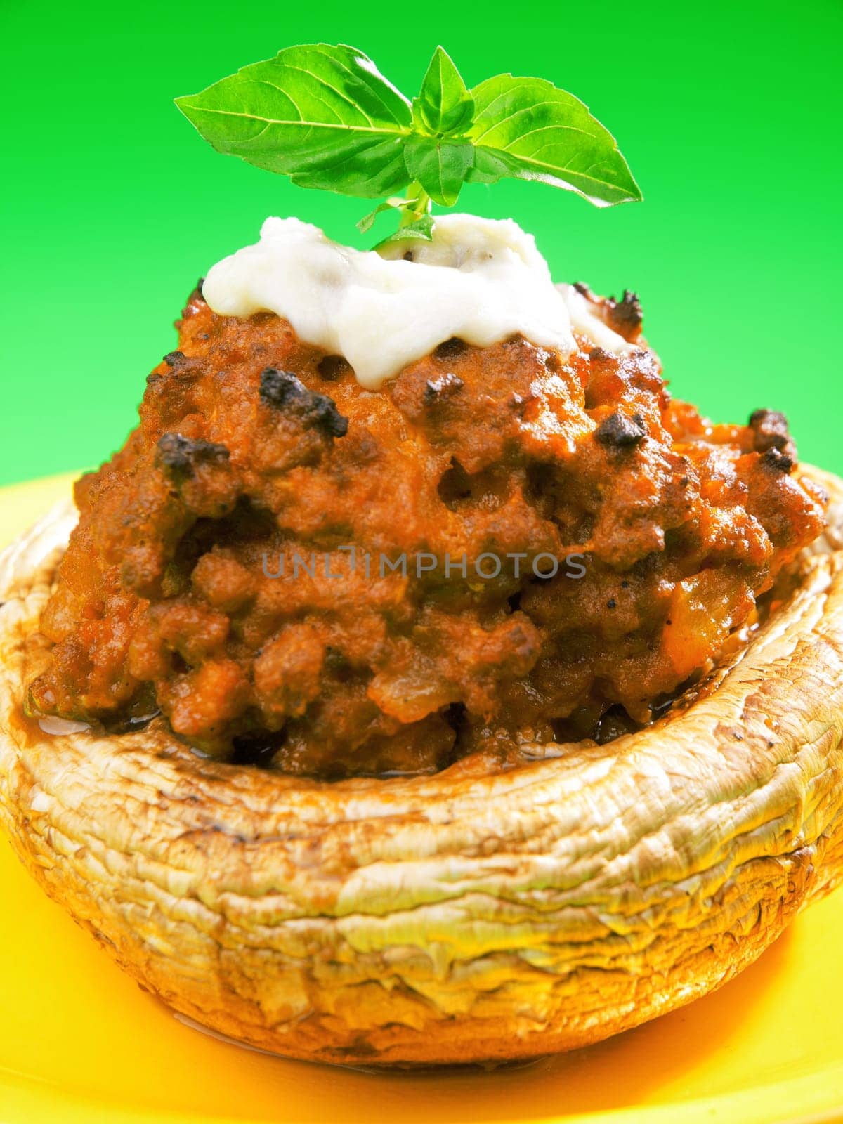 Stuffed mushrooms with meat and mozzarella decorated with fresh basil, izolated on green background