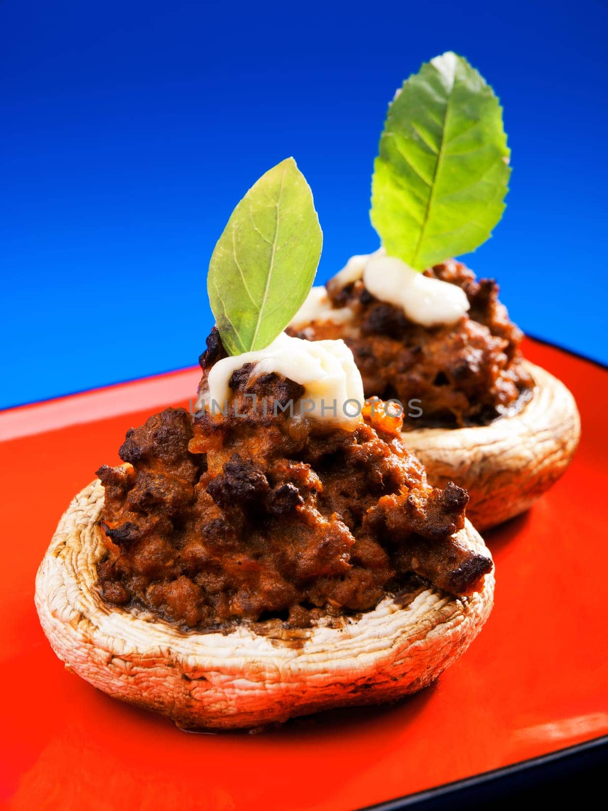 Stuffed mushrooms with meat and mozzarella decorated with fresh basil, izolated on green background