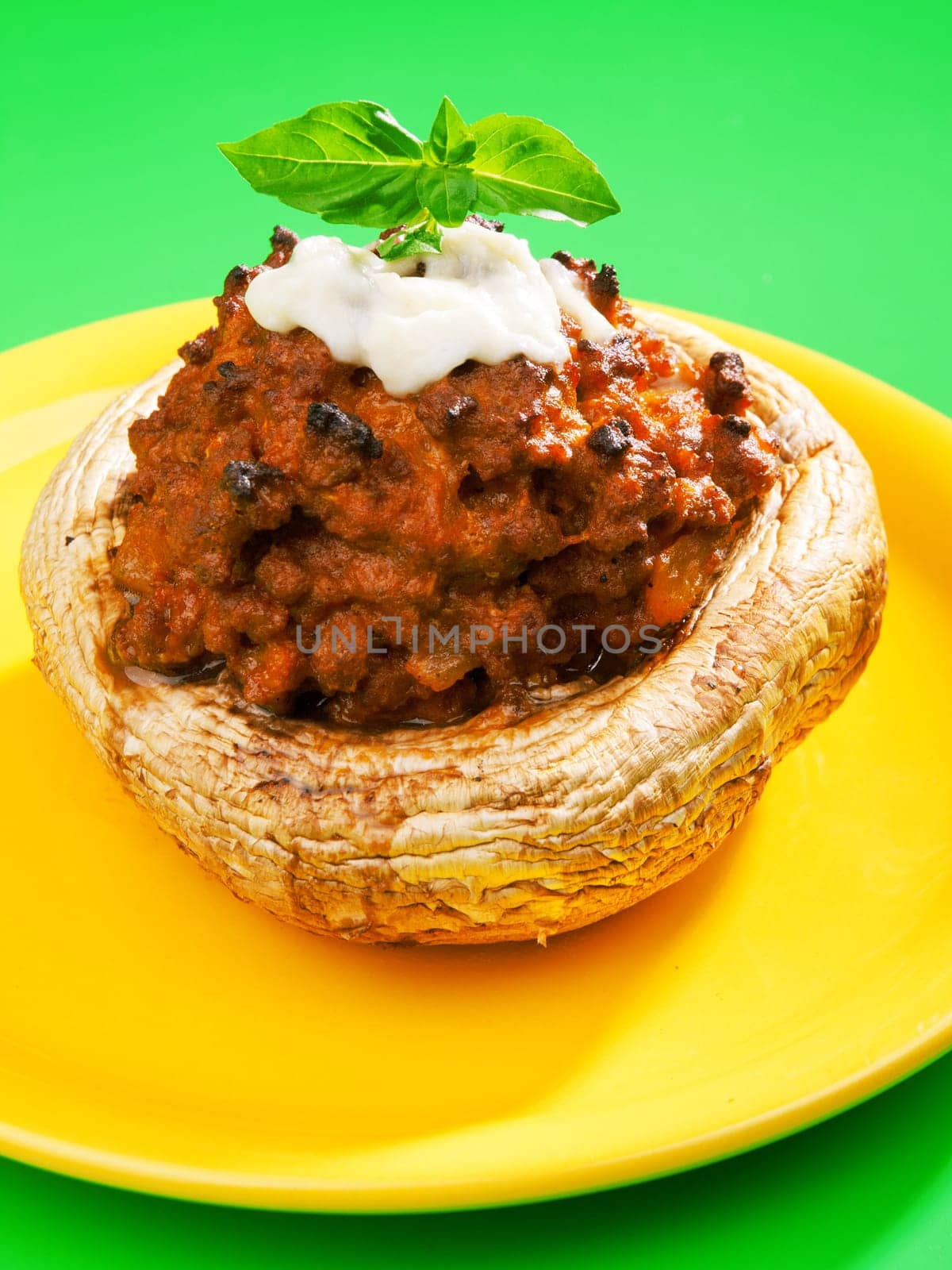 Stuffed mushrooms with meat and mozzarella decorated with fresh basil, izolated on green background
