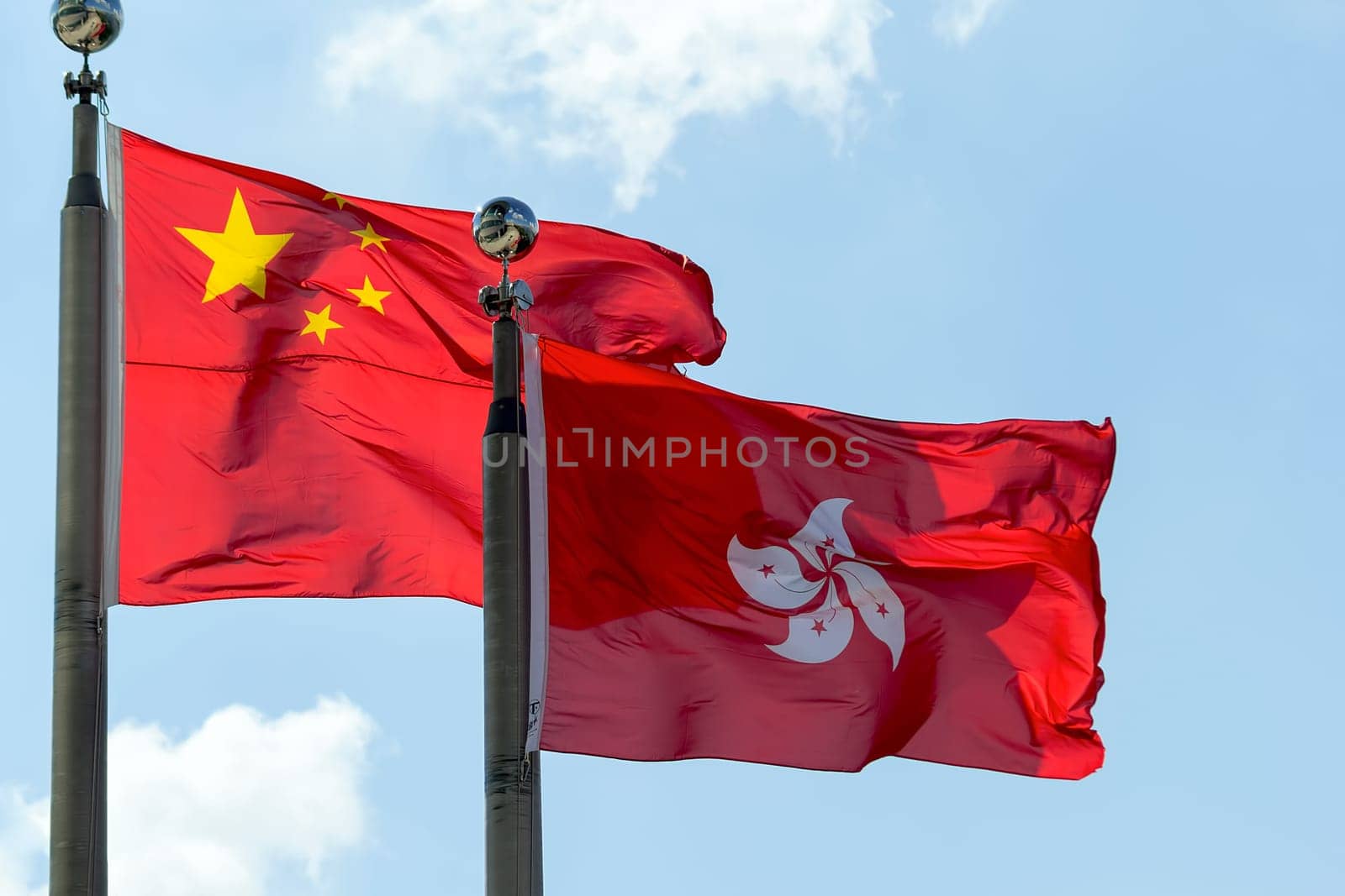 Hong Kong and Peoples Republic of China Flags Flying Side by Side Against Blue Sky