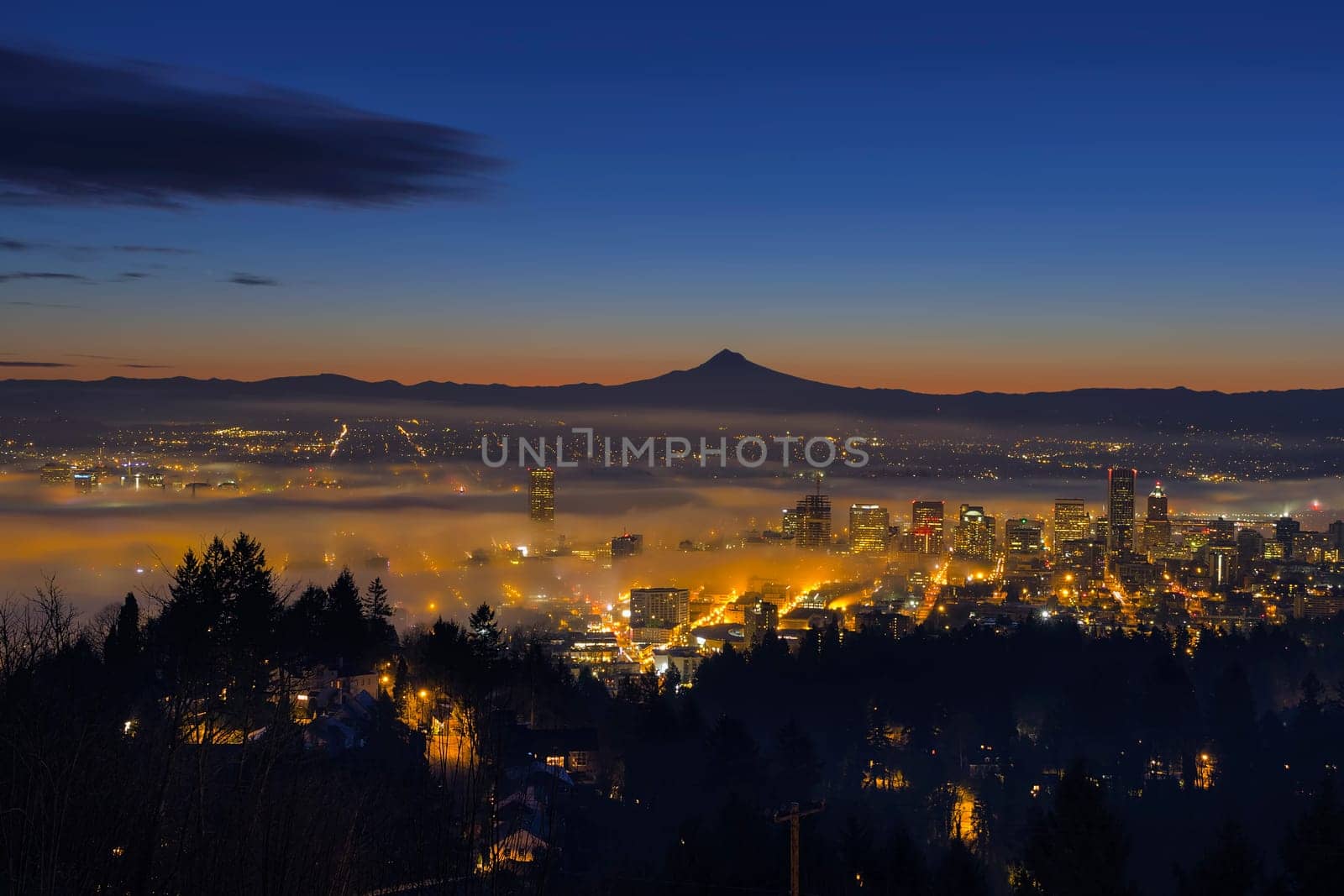 Thick Fog Rolling at Dawn over cityscape of downtown Portland Oregon with city lights and silhouette of Mt Hood