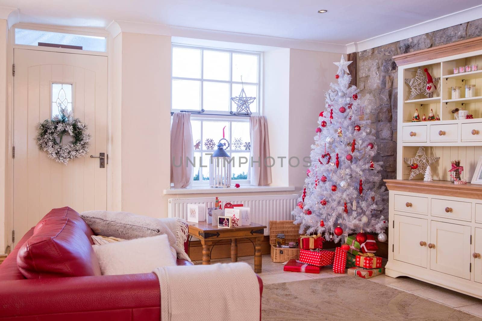 A Horizontal Image of a Living Room dressed for Christmas. Colours mainly Red and White and spacious. No People.