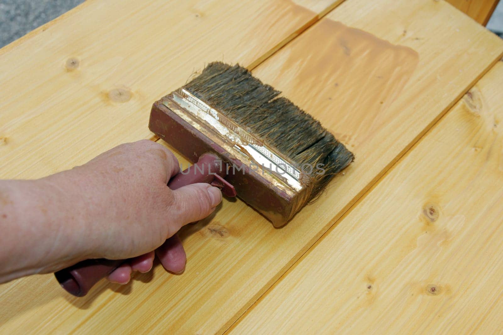 A woman strokes wood protection glaze on boards with a brush