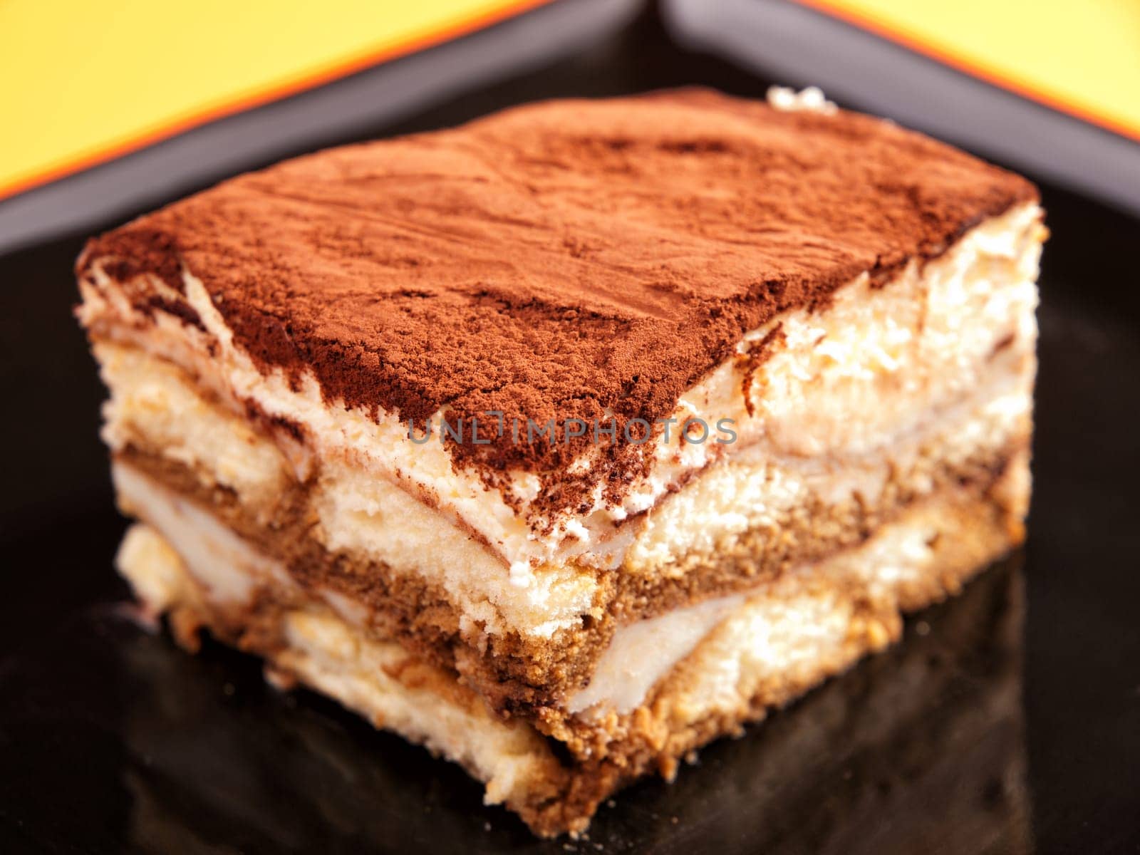 Tiramisu cake in a black plate, close up