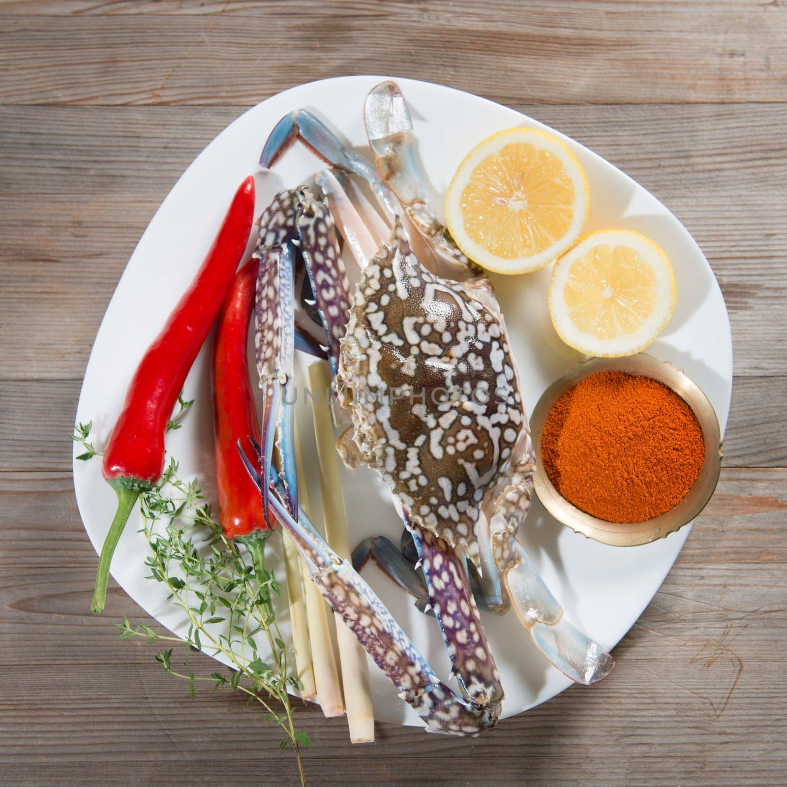 Top view raw blue crab and ingredients ready to cook, on white plate.