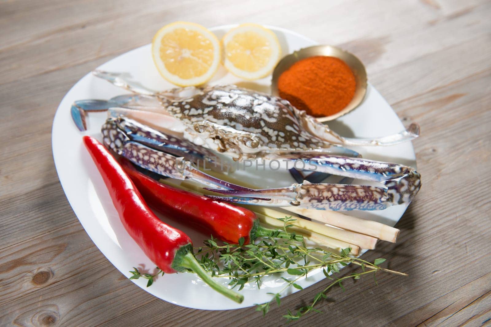 Raw blue crab and ingredients ready to cook, on white plate.