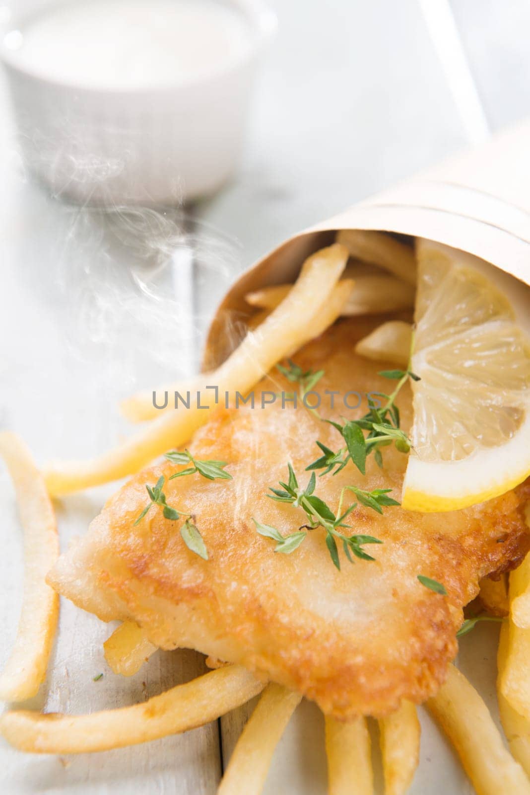 Fish and chips. Fried fish fillet with french fries wrapped by paper cone, on wooden background. Fresh cooked with hot steams.