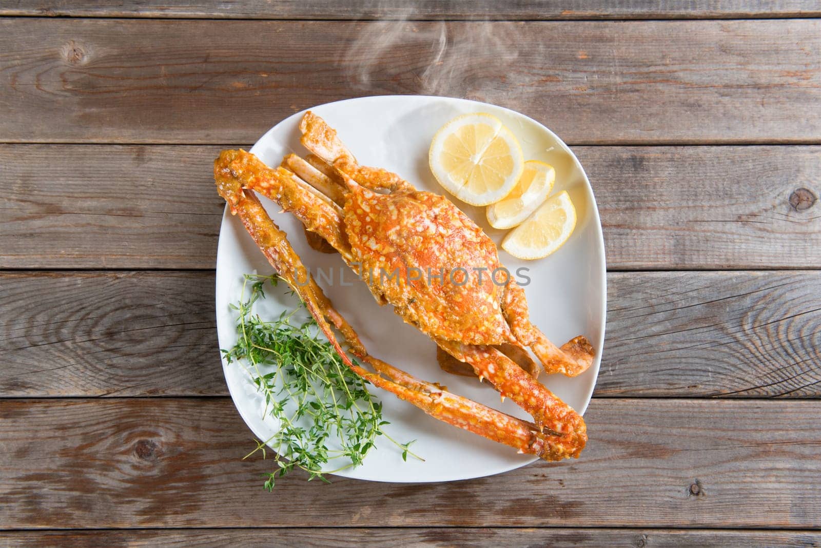 Top view cooked delicious hot and spicy sauce blue crab on white plate, at wood background. Fresh cook with hot smoke steams.