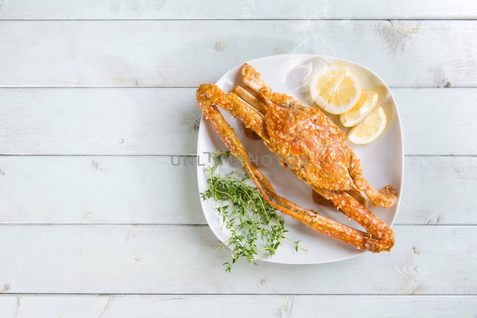 Top view cooked delicious hot and spicy sauce blue crab on white plate, at bright wooden background. Fresh cook with hot smoke steams.