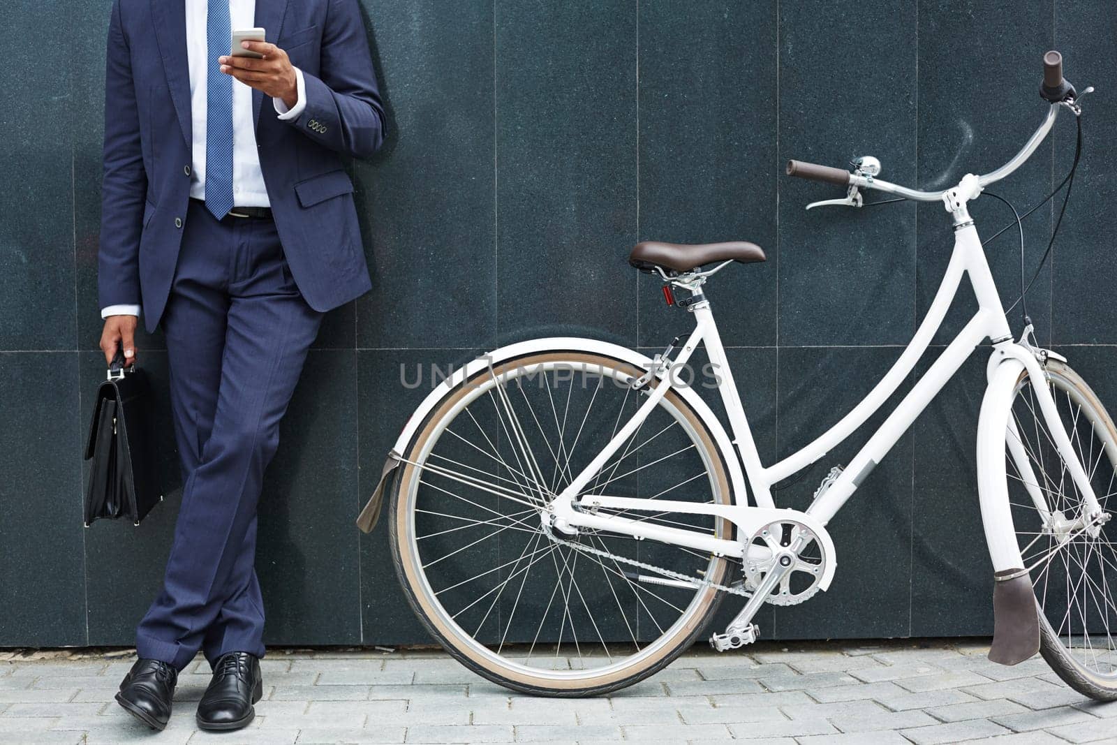 Close-up of modern businessman with cellphone standing by wall of modern building with bicycle near by