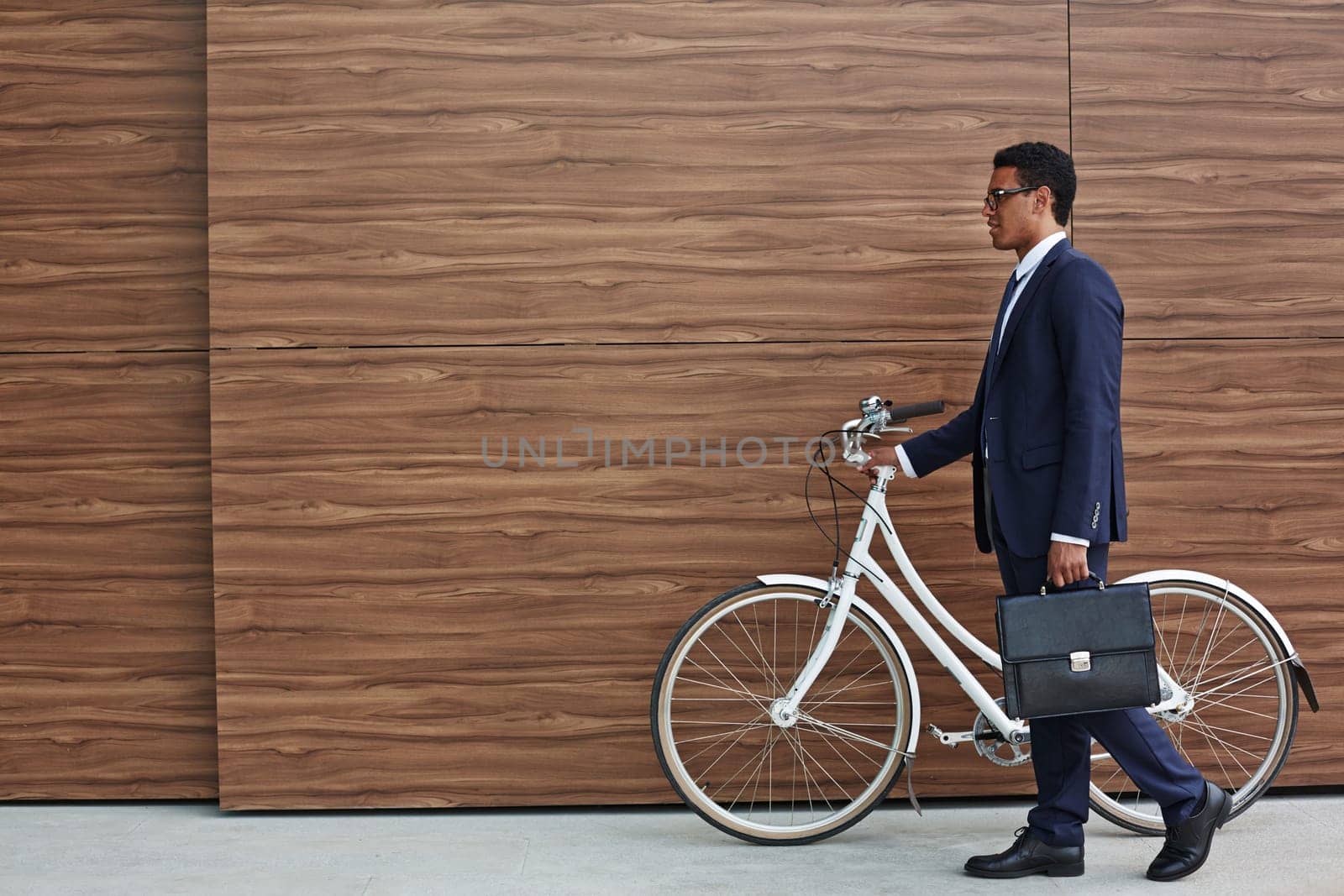 Businessman with briefcase and bicycle walking along wooden wall