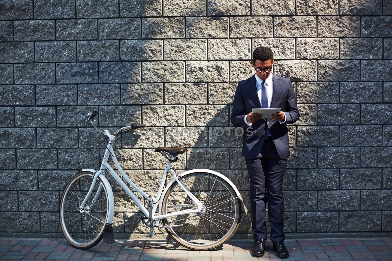 Handsome employee with touchpad networking by wall of modern building with bicycle near by