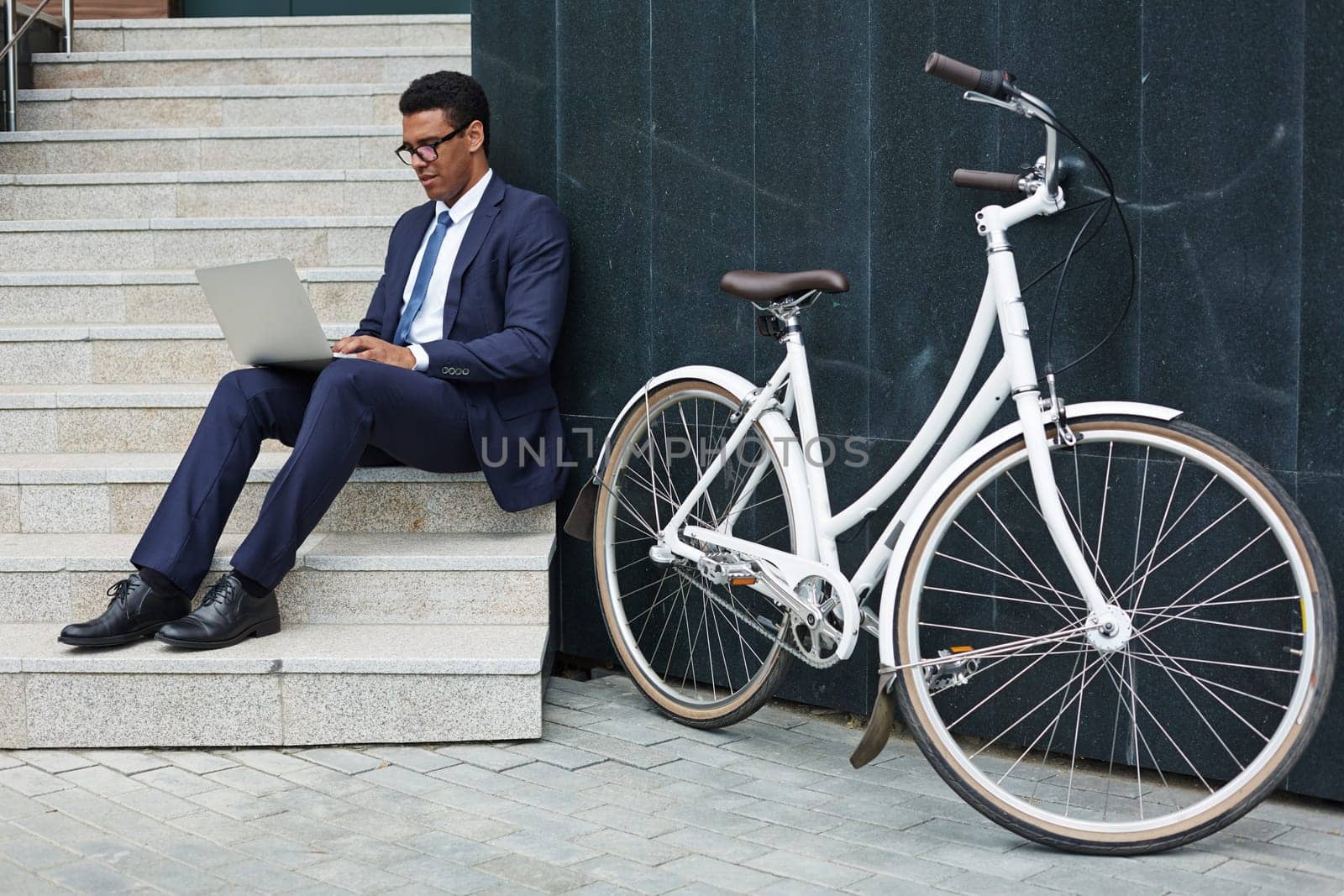 Handsome employee sitting on stairs and typing on laptop