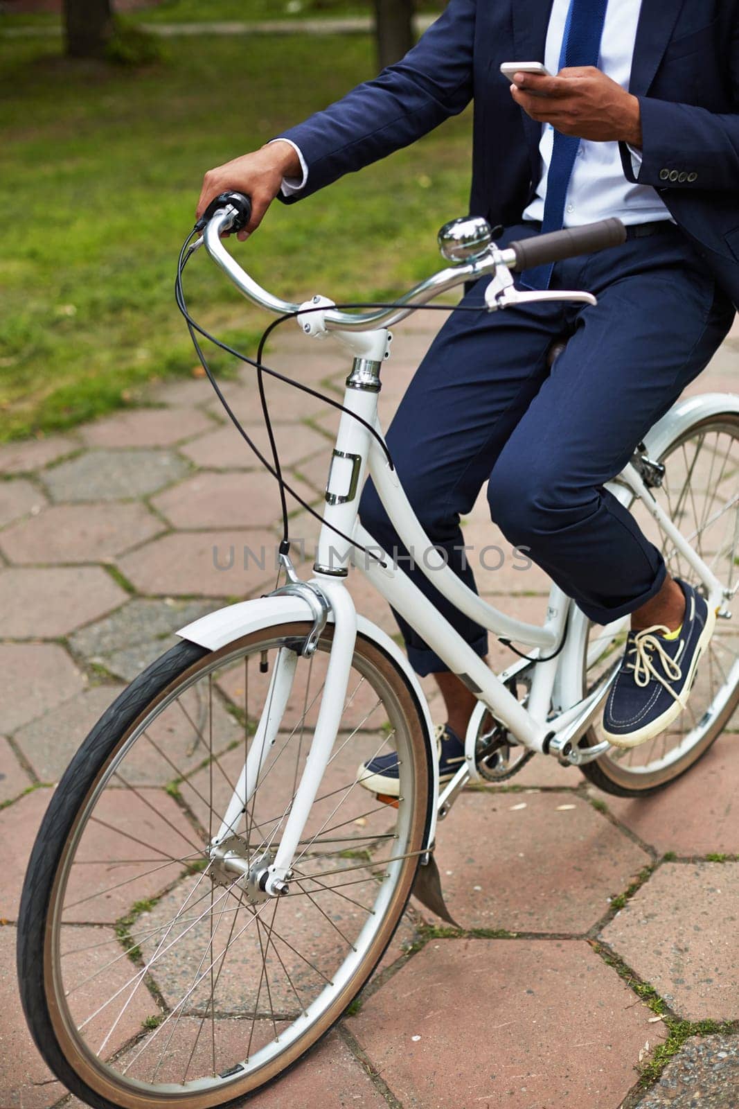 Modern and active businessman with cellphone riding bicycle in park