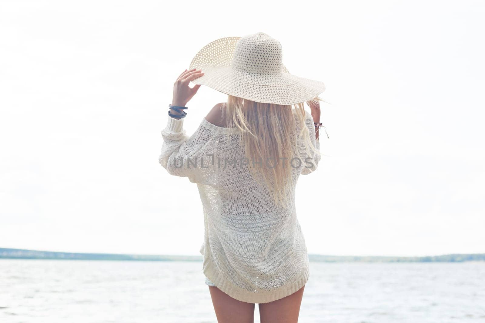 Young woman in hat and white pullover having rest by the sea