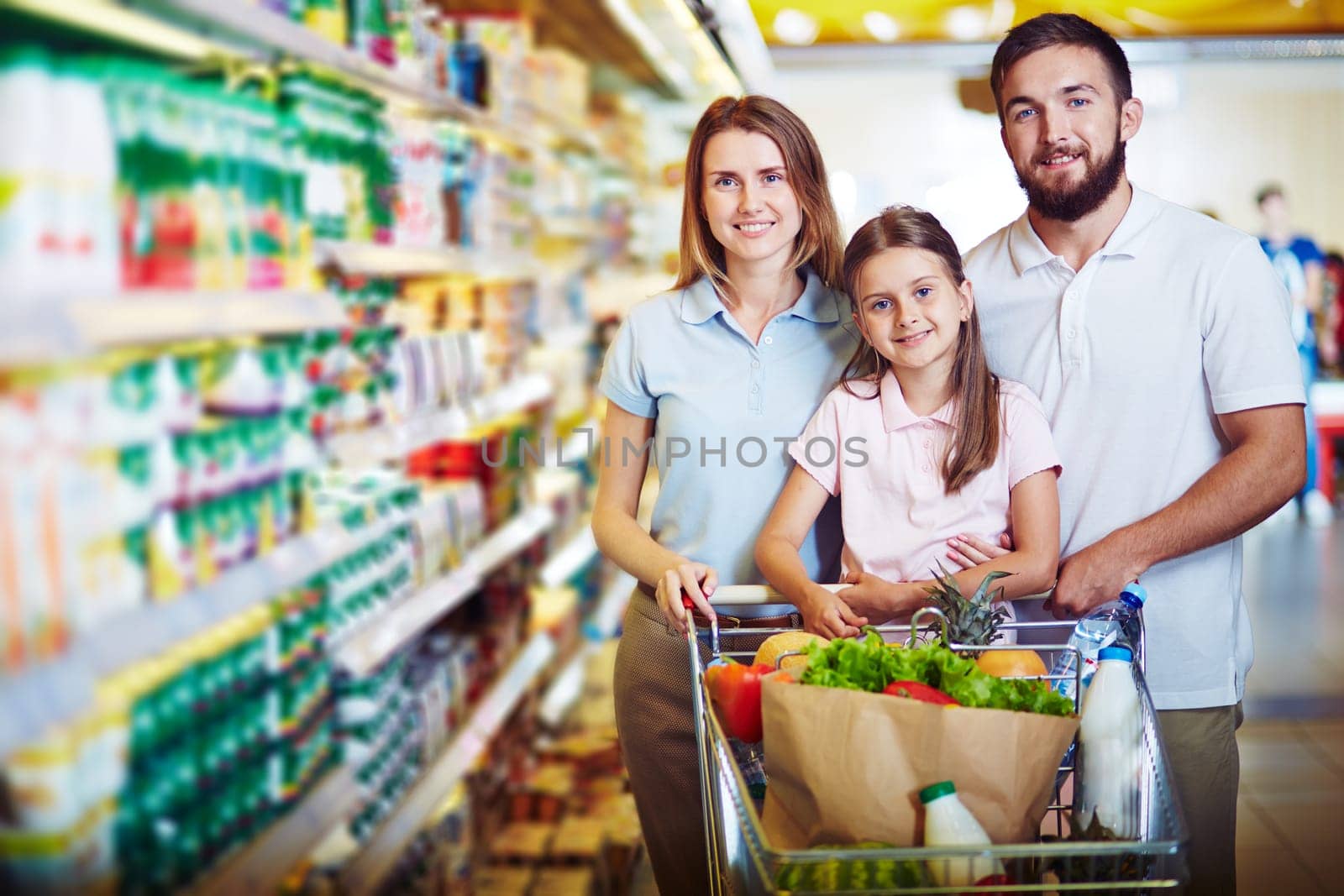 Modern family looking at camera while buying food in supermarket