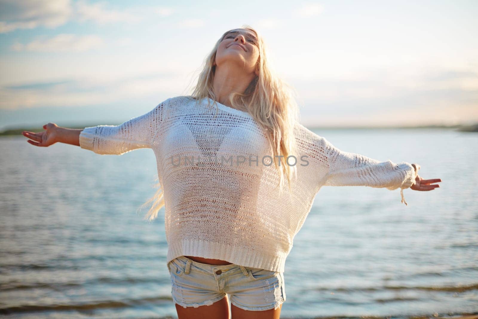 Delighted blond girl in white pullover and denim shorts enjoying her summer vacation by the sea