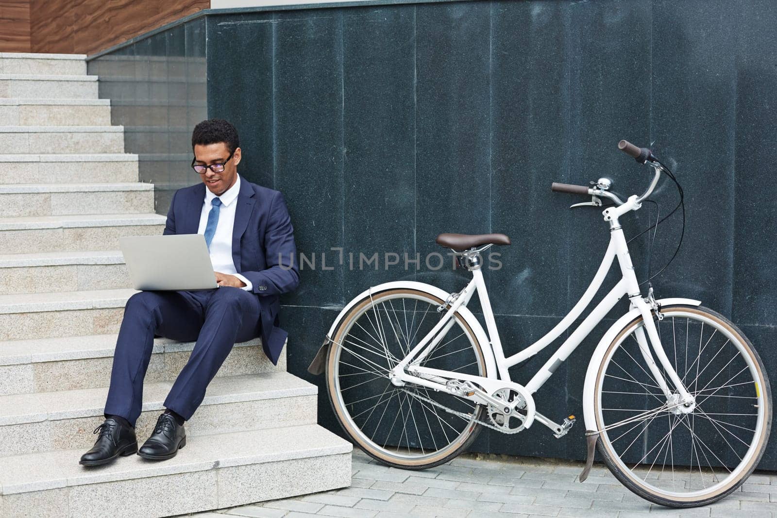 Modern employee sitting on stairs and networking outdoors