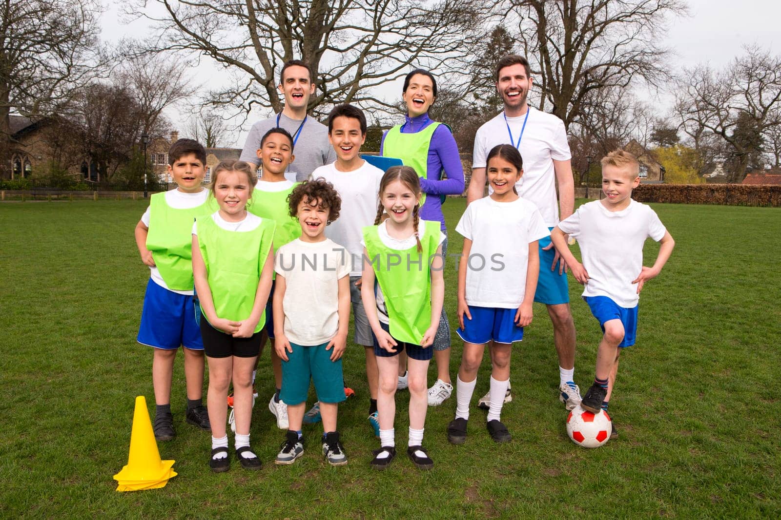 A group portrait of a kids soccer team, behind them are their coaches. They are all smiling and look happy.