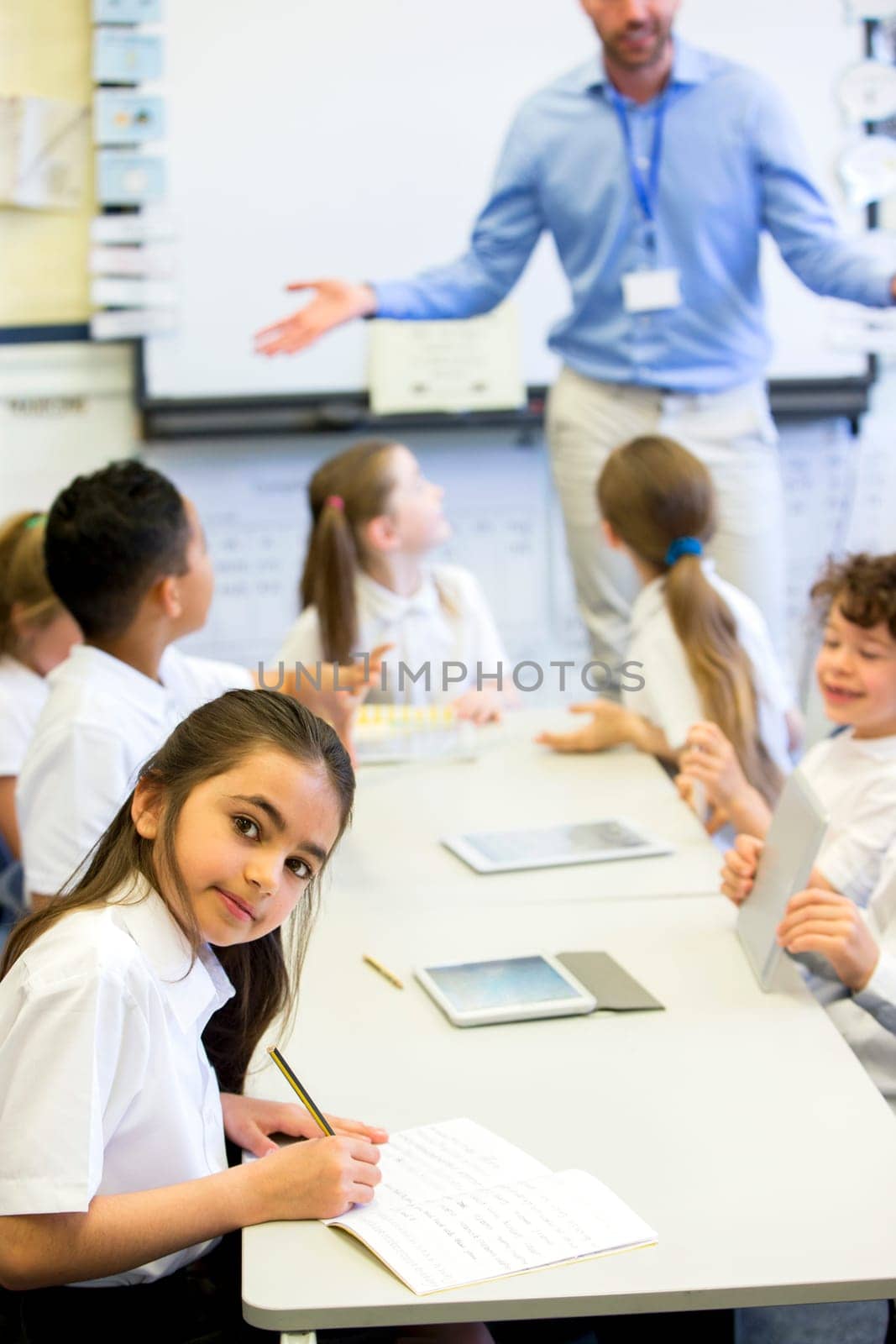 School girl smiles at the camera as she sits at her desk while working.