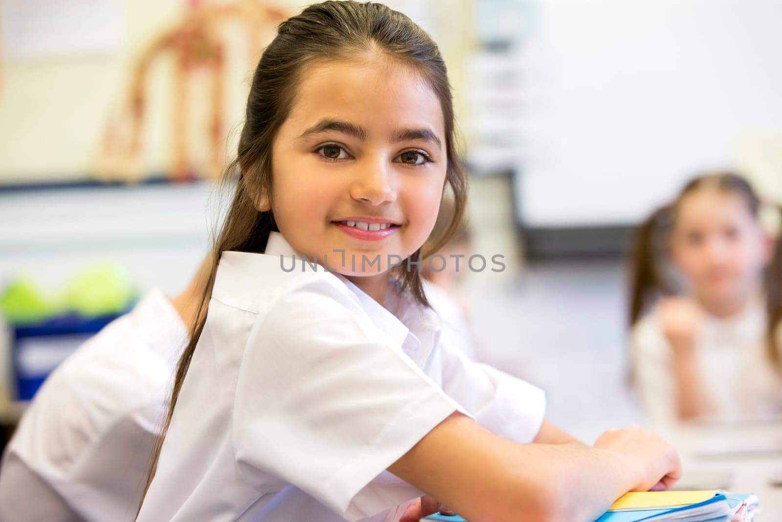 School girl smiles at the camera as she sits at her desk while working.