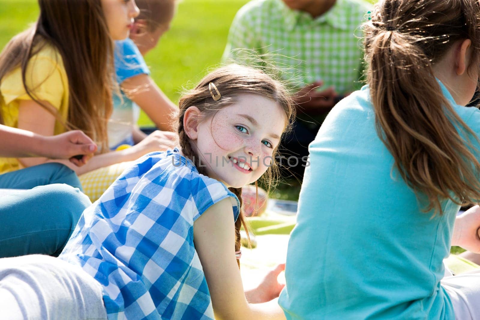 Small group of school children having a class outdoors. A girl turns her head to look behind into the camera and smiles.