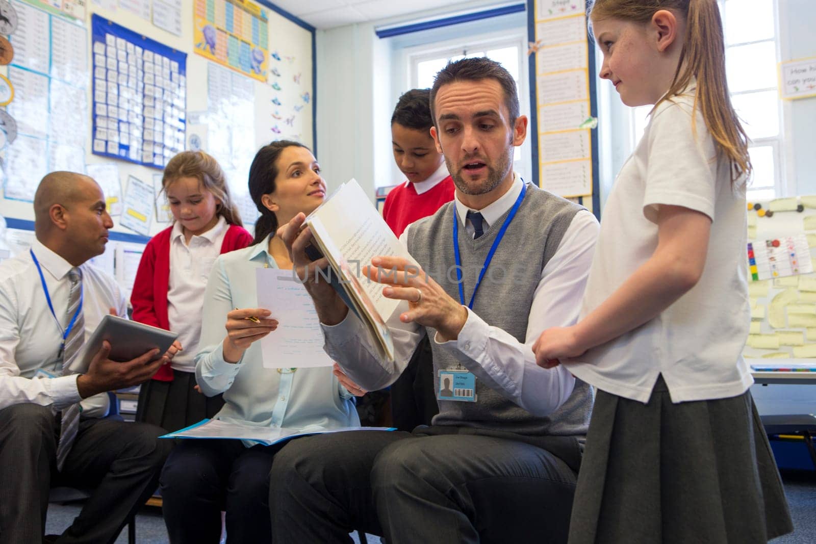 Some students each sit with a teacher practising and learning to read at the front of the class.