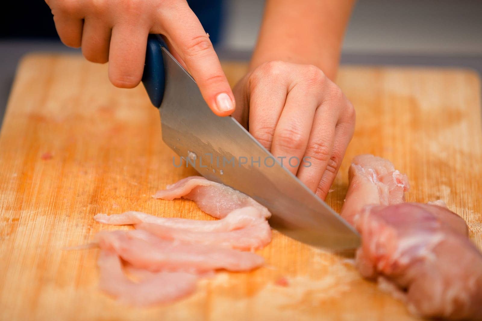 Young woman cutting meat for cooking with knife