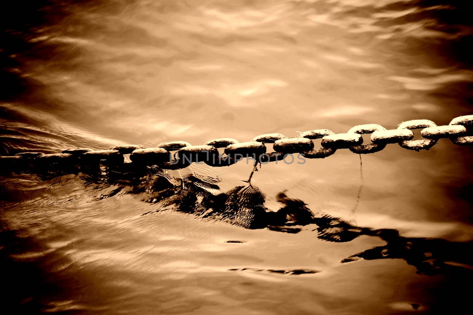 The bizarre and brute ton of an anchor chain protruding from a body of water.