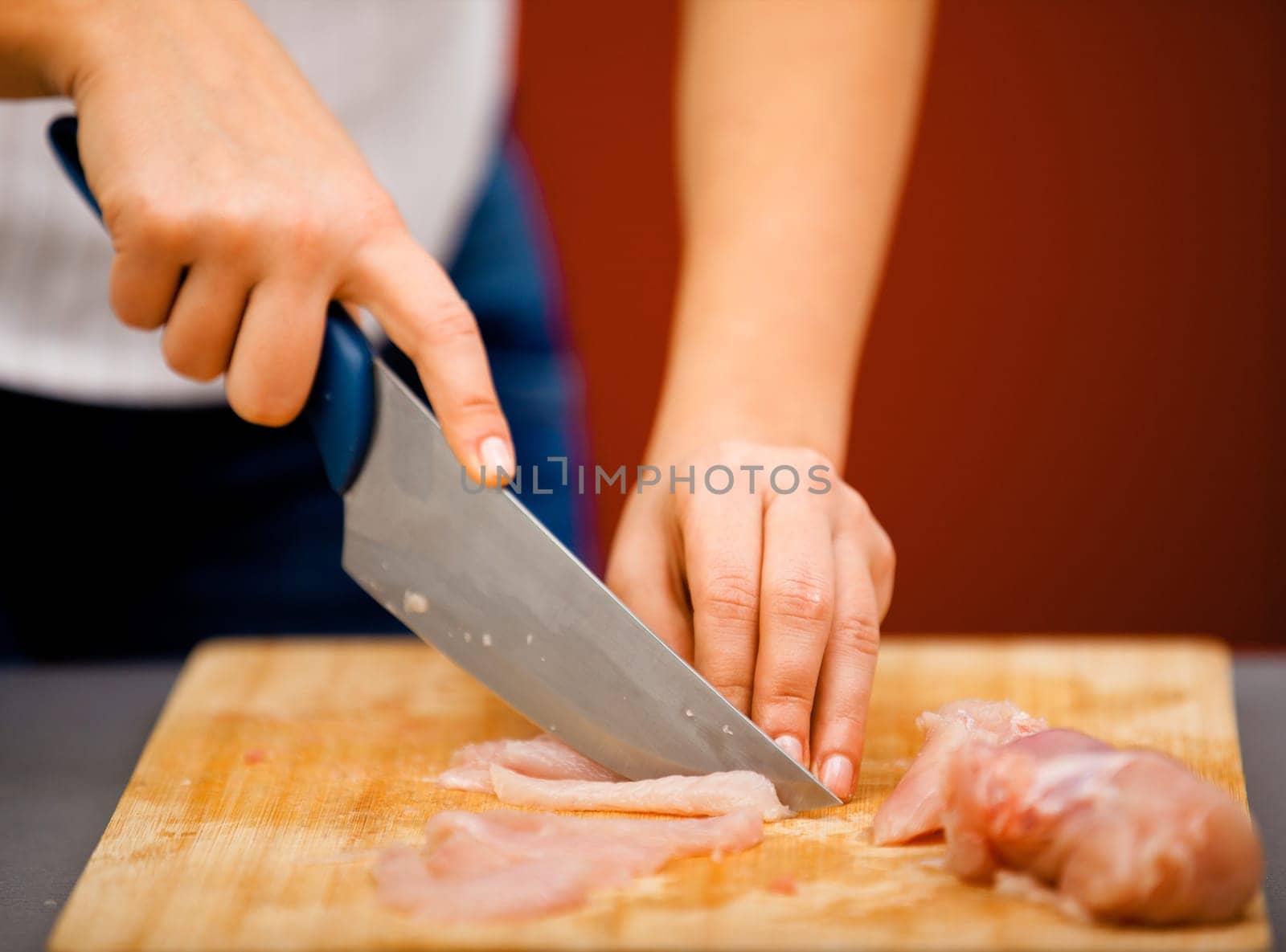 Young woman cutting meat for cooking with knife