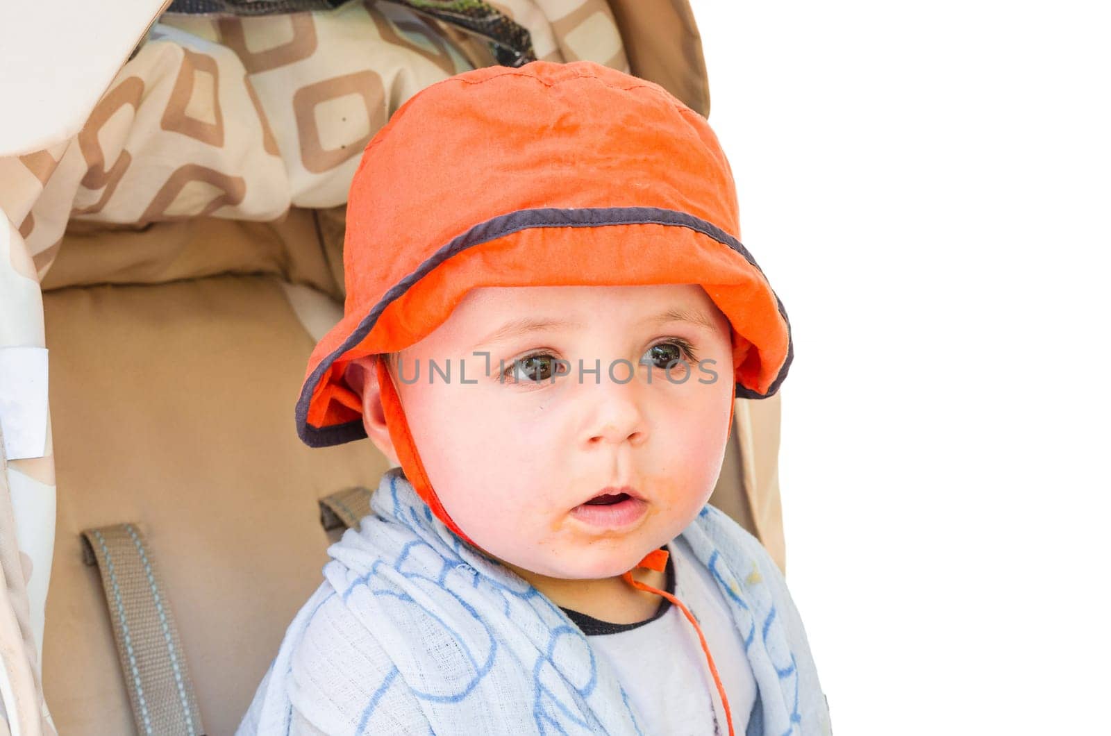 Baby with orange cap sits in the pram and looks astonished. Background is exempted.