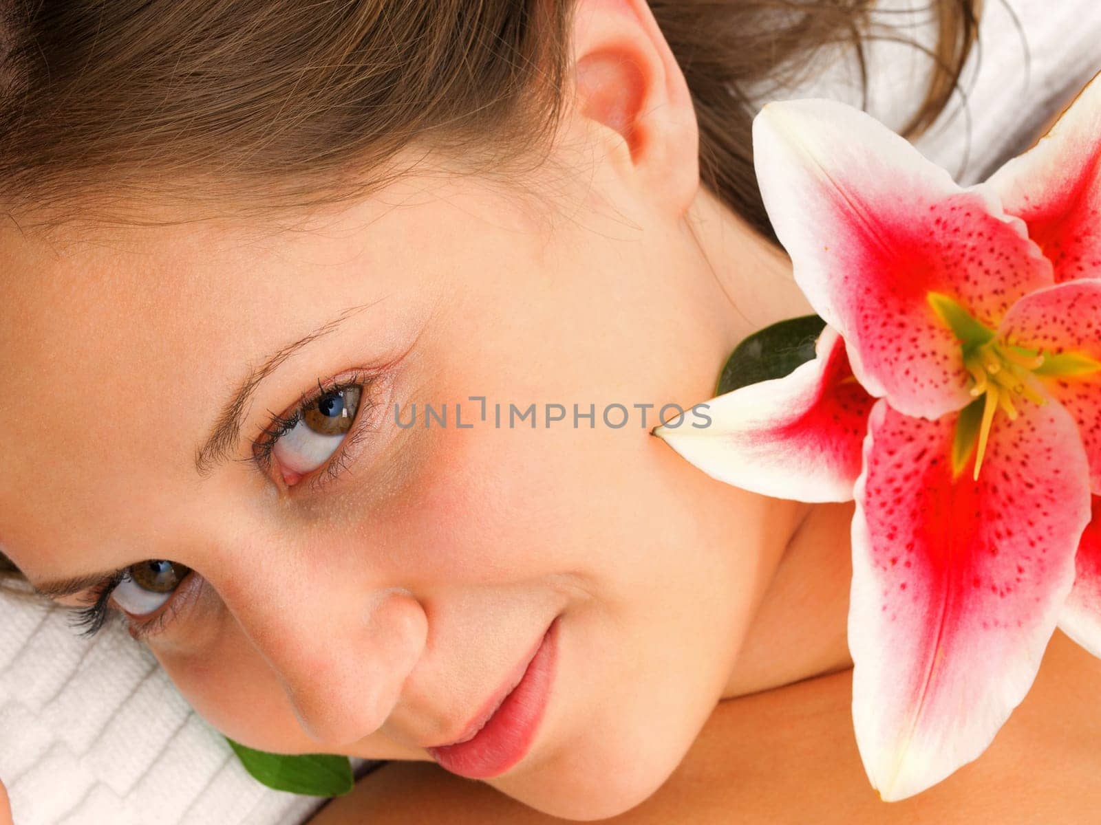 Young woman lying on white background with flowers in her hair waiting in spa studio for massage