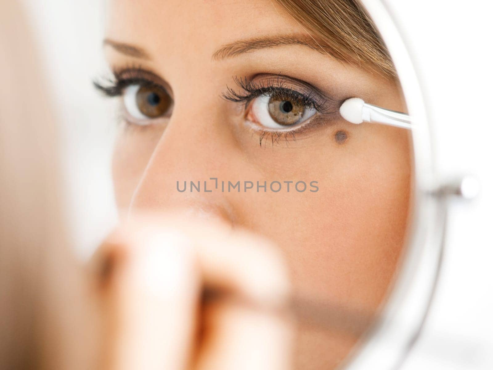 Applying make-up on young woman face, reflection in the mirror