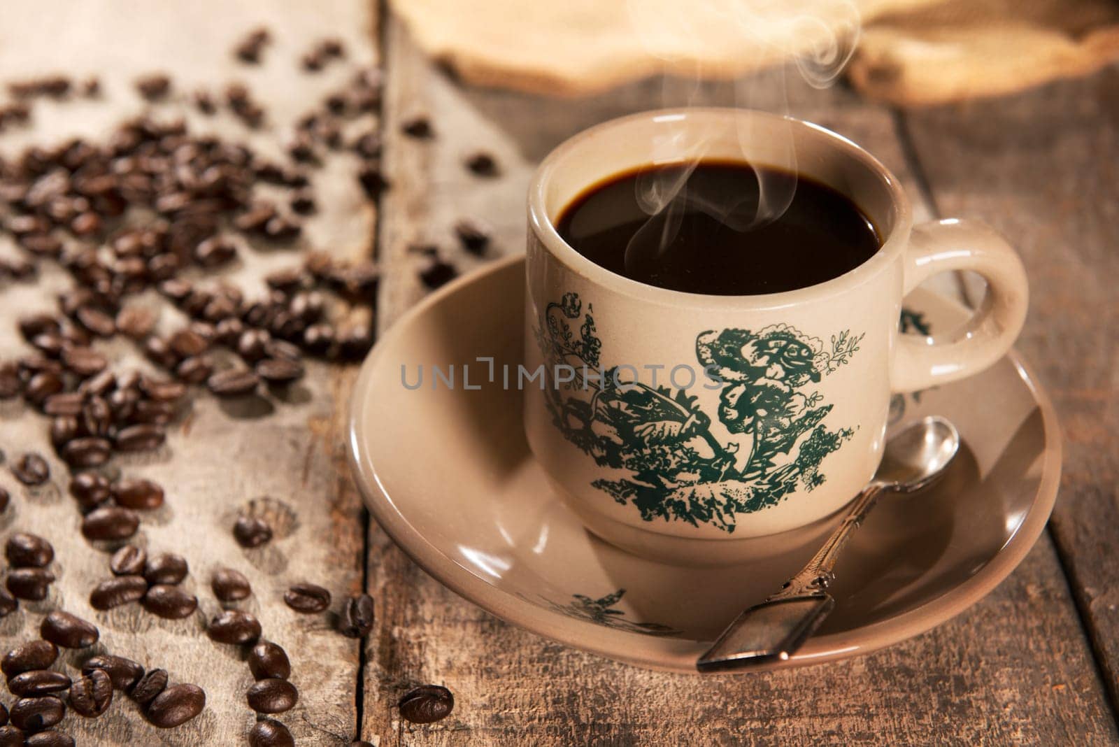Steaming traditional Chinese Hainan style coffee in vintage mug and saucer with coffee beans. Fractal on the cup is generic print. Soft focus setting with dramatic ambient light on dark wooden background.