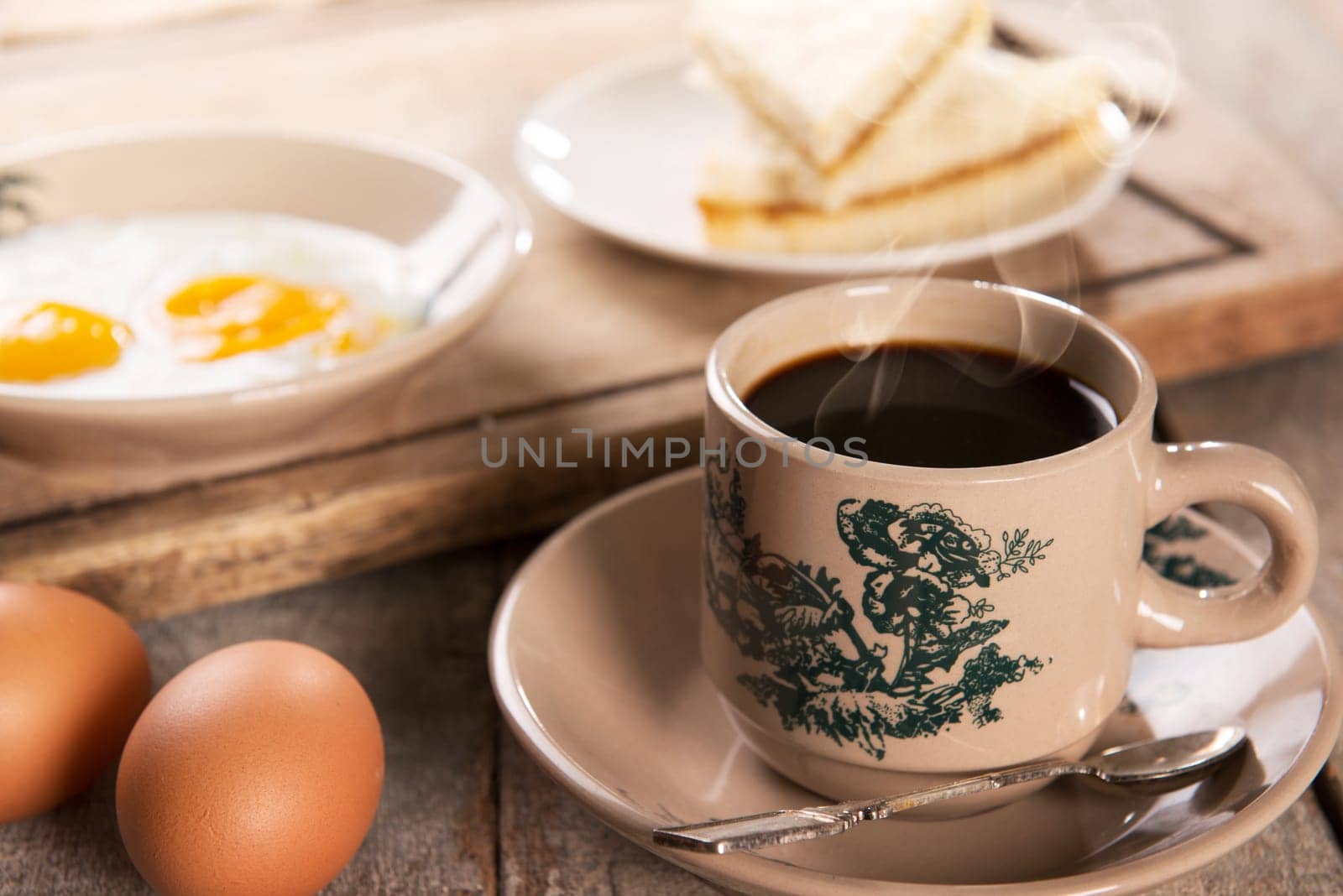 Traditional Singaporean Chinese style coffee in vintage mug and saucer with breakfast. Fractal on the cup is generic print. Soft focus dramatic ambient light over wood table.