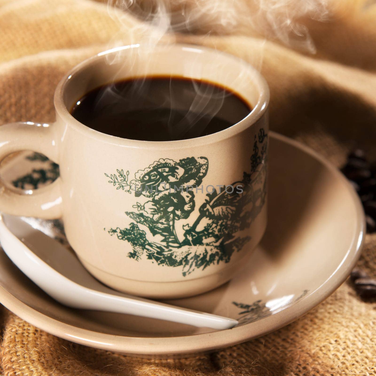 Steaming traditional oriental Chinese kopitiam style dark coffee in vintage mug and saucer. Fractal on the cup is generic print. Soft focus setting with dramatic ambient light on dark wooden background.