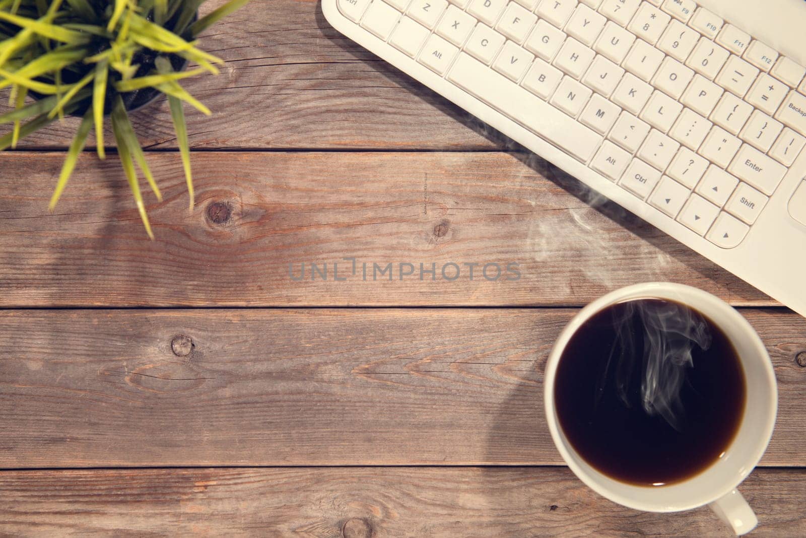 Top view work space with computer keyboard, cup of coffee and plant pot. Wooden table background in vintage toned.