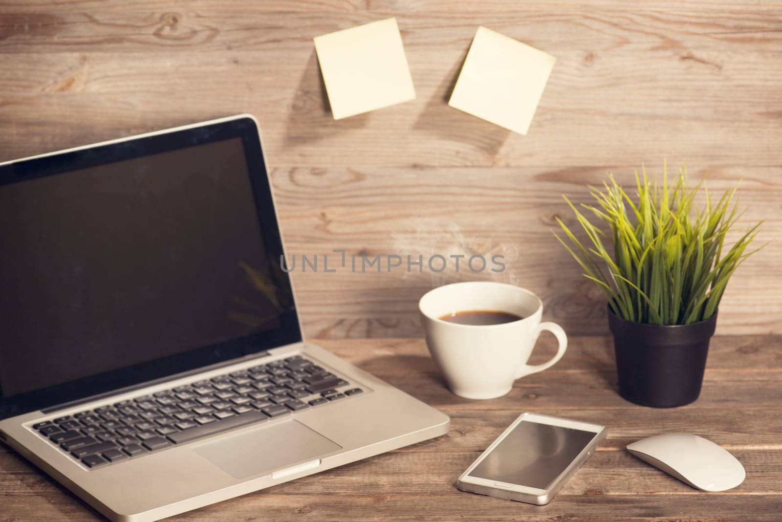 Wooden working desk with laptop, cup of hot coffee, mouse, smartphone and pot plant, in vintage toned.