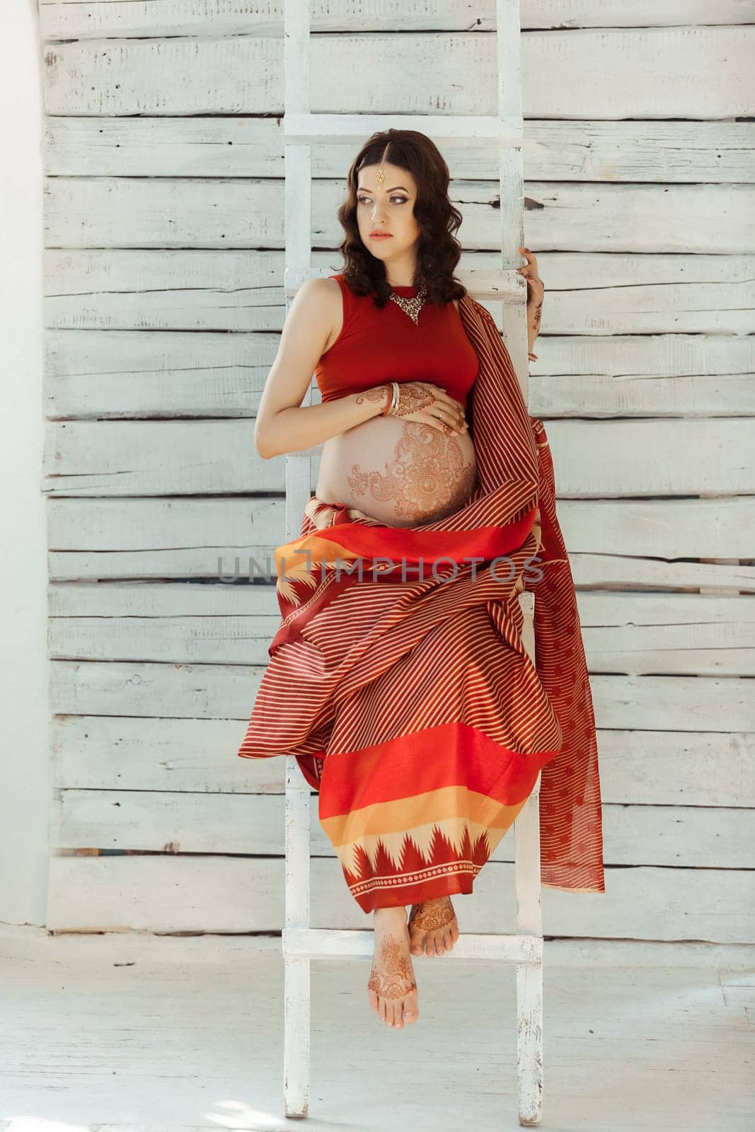 Indian picture on woman mehendi tradition decoration, resistant design by special paint, brown henna. Woman sitting in indian red dress on white wooden staircase background