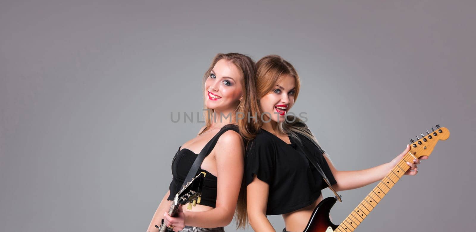 Two beautiful girls  with long hair playing guitars in rock style on a gray background