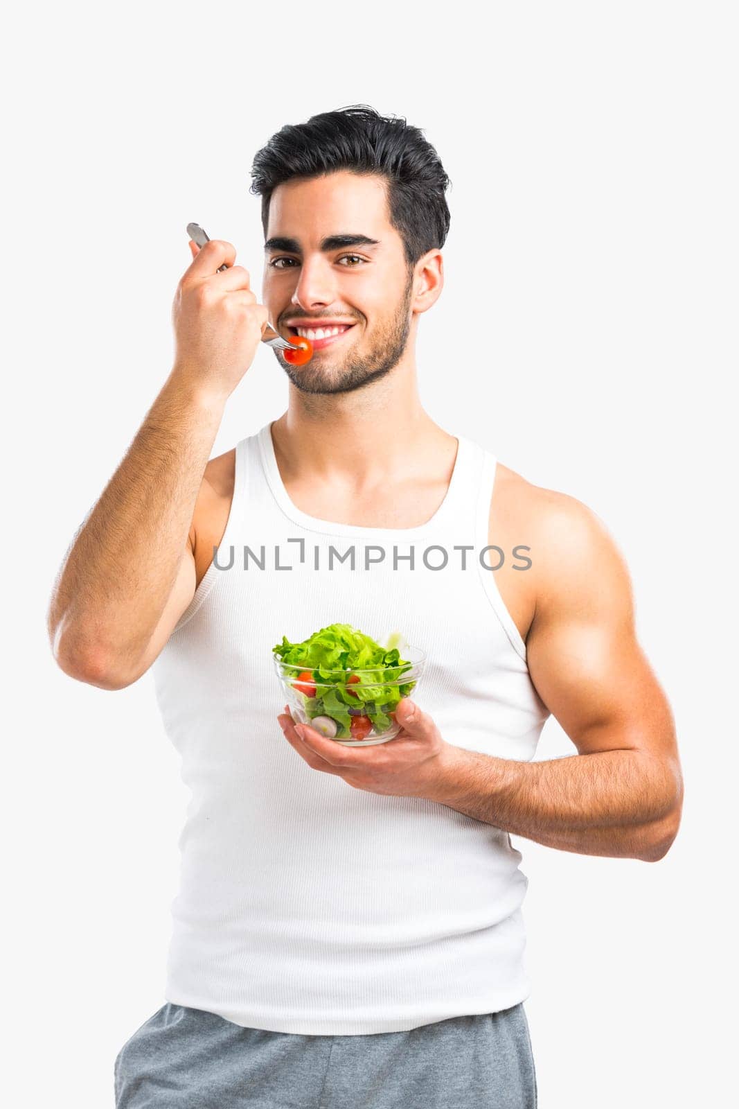 Handsome young man eating a healthy salad, isolated over a gray background