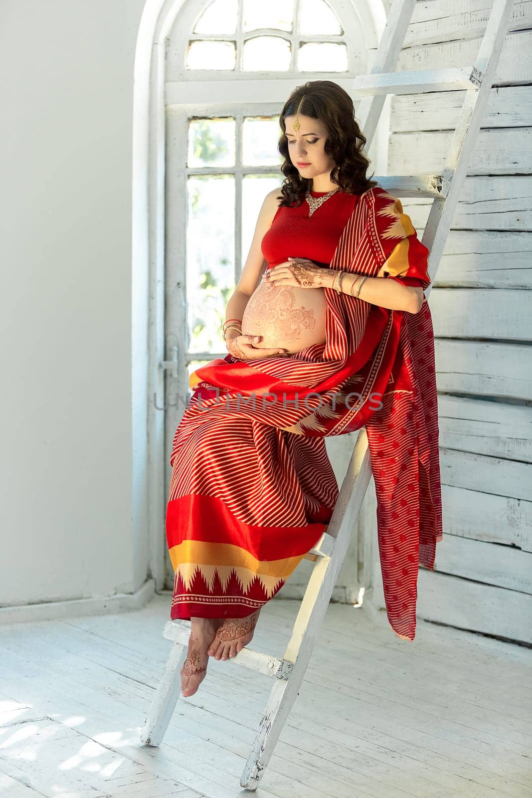 Indian picture on woman mehendi tradition decoration, resistant design by special paint, brown henna. Woman sitting in indian red dress on white wooden staircase background