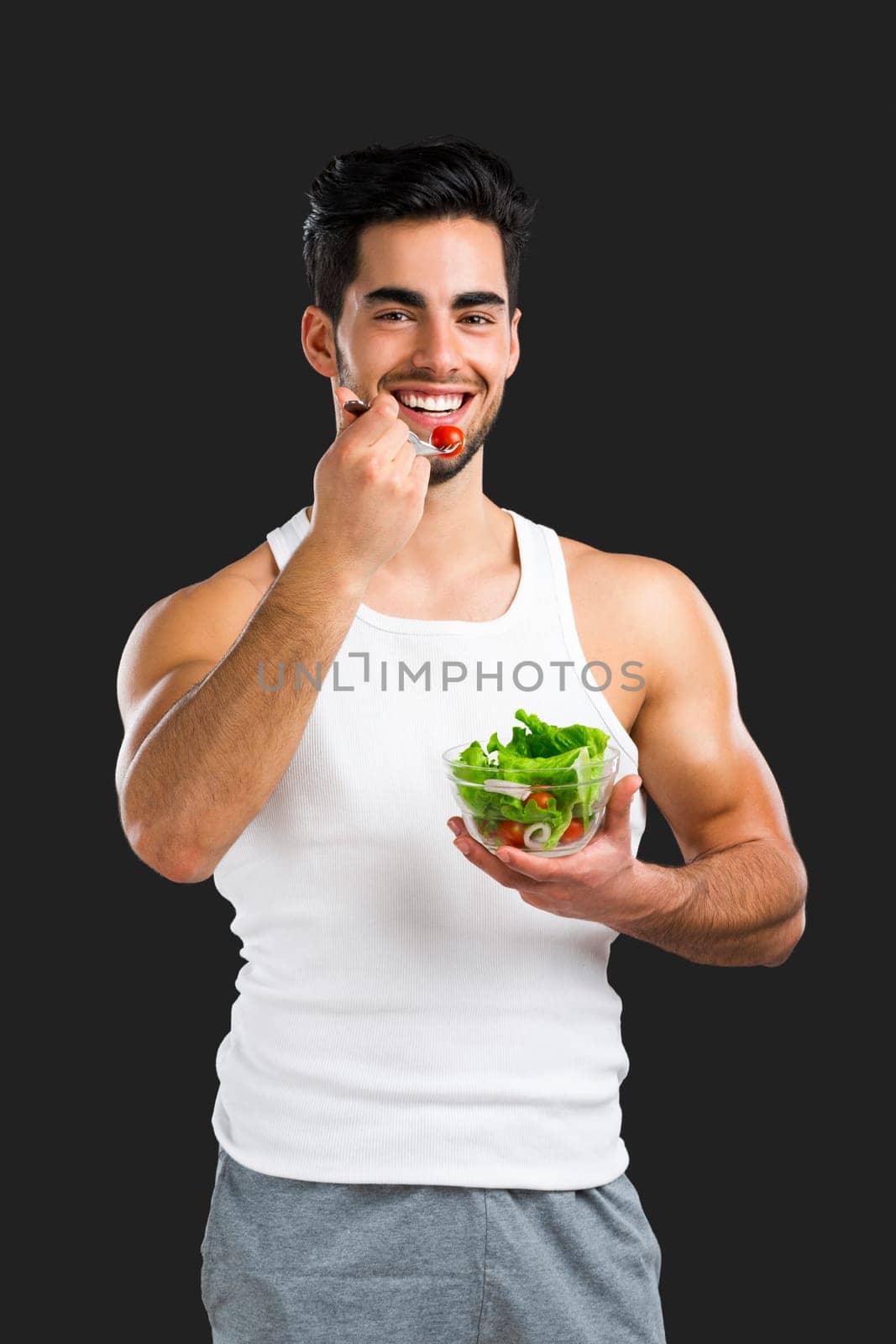 Handsome young man eating a healthy salad, isolated over a gray background