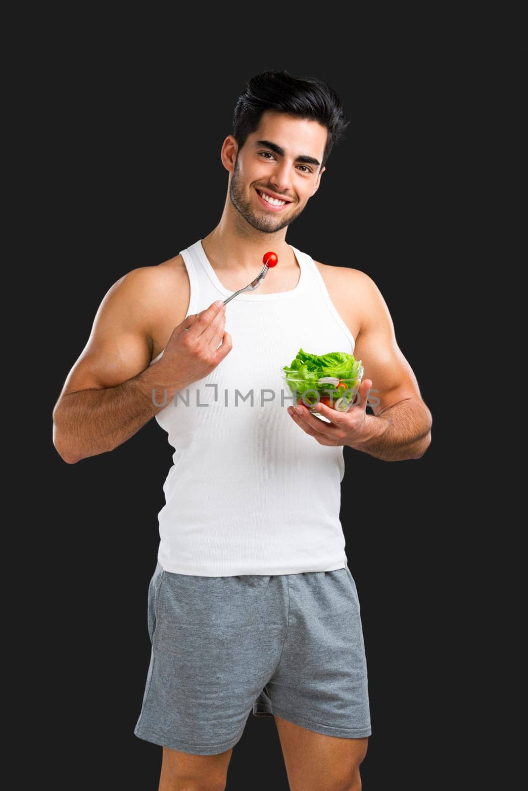 Handsome young man eating a healthy salad, isolated over a gray background