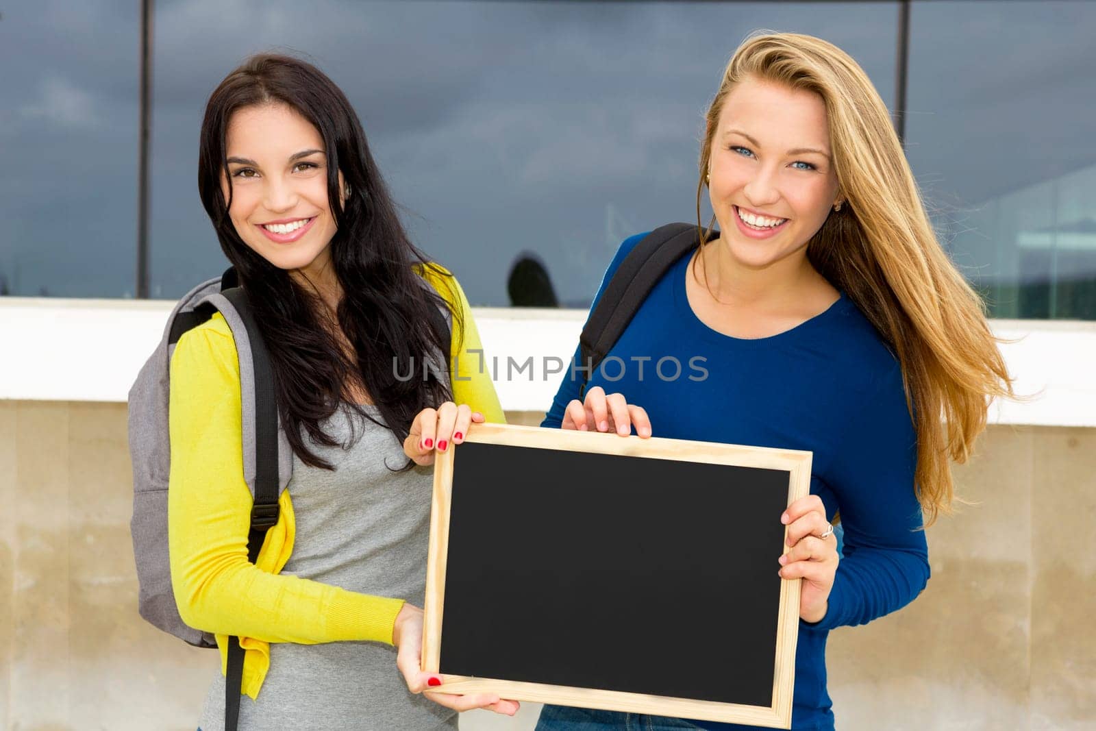 Two beautiful teenage students holding backpacks and smiling