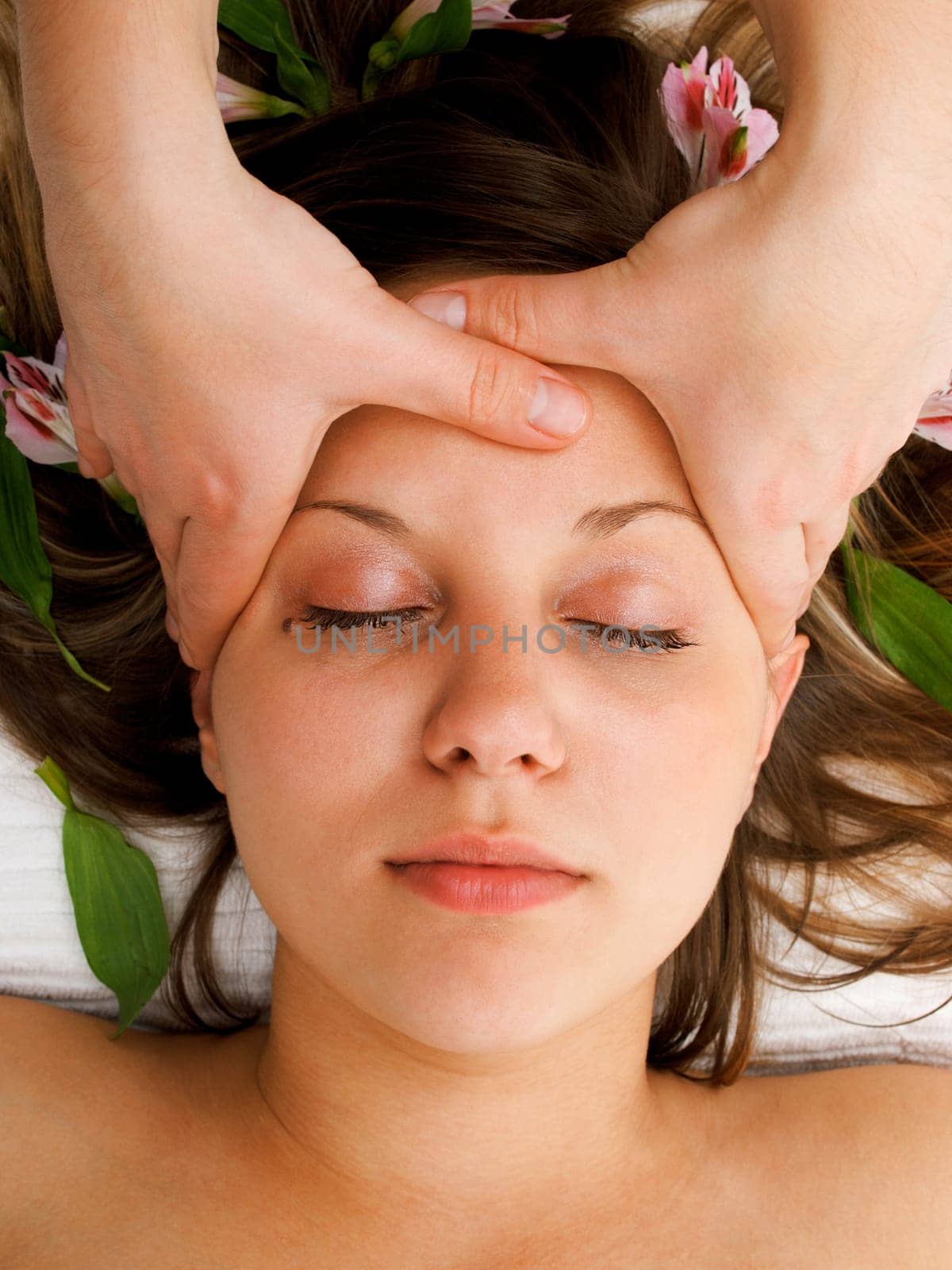 Young woman lying on white background with flowers in her hair waiting in spa studio for massage