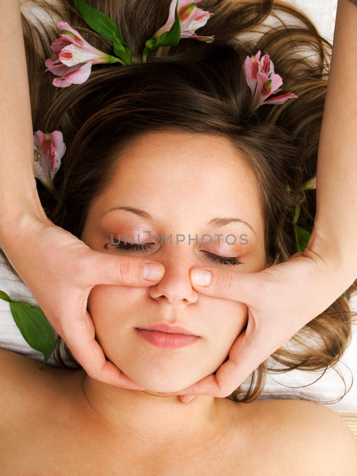 Young woman lying on white background with flowers in her hair waiting in spa studio for massage