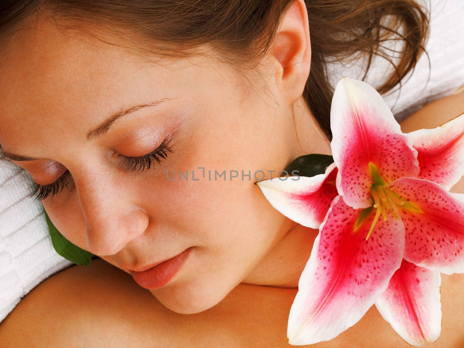 Young woman lying on white background with flowers in her hair waiting in spa studio for massage