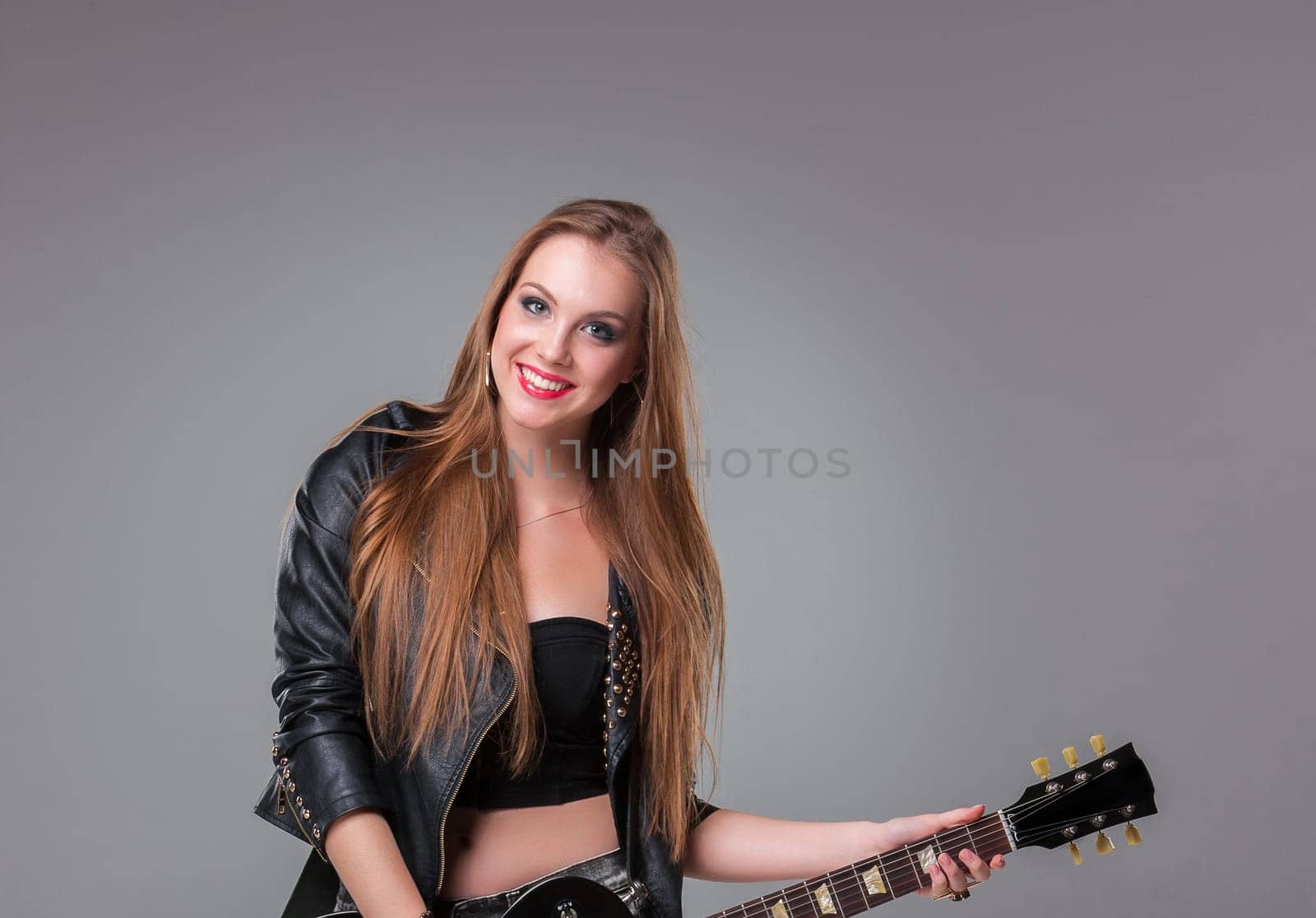 Beautiful girl  with long hair playing guitar in rock style on a gray background