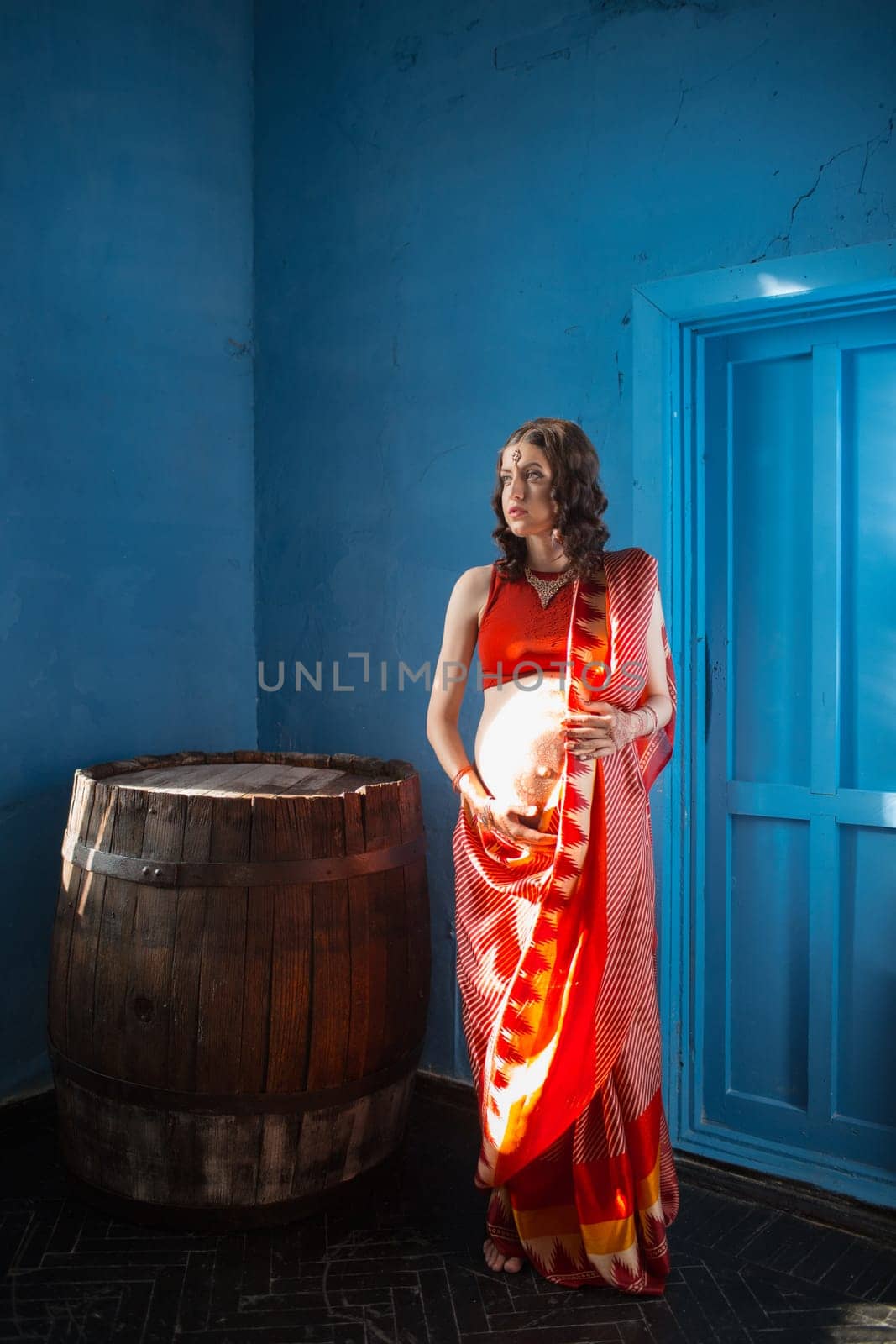 Indian picture on woman hands and pregnant belly with henna tattoo on blue wall background